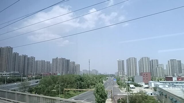 A window view from a moving high-speed train passing through a dense urban residential area with rows of modern high-rise apartment buildings in Zhengzhou, China.