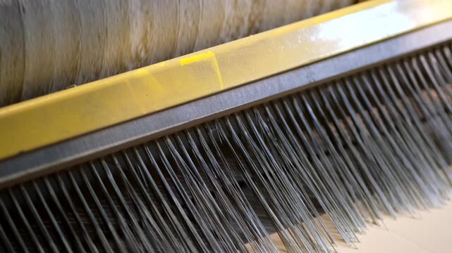 Macro shot of fine synthetic bristles or brush fibers attached to a metal beam above a machine roller.