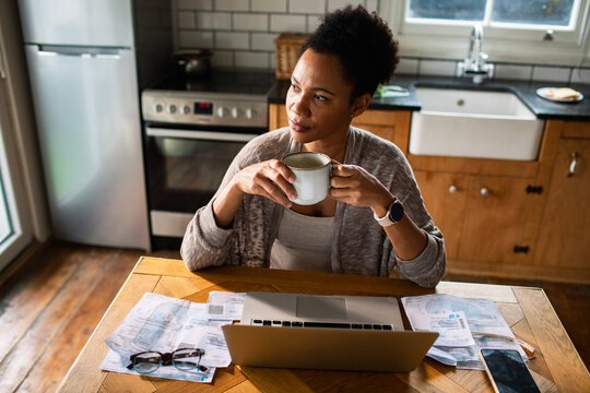 Woman managing finances at kitchen table with laptop