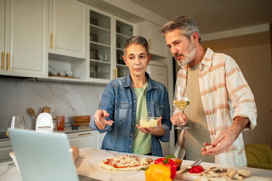 Mature couple cooking homemade pizza in home kitchen during online class