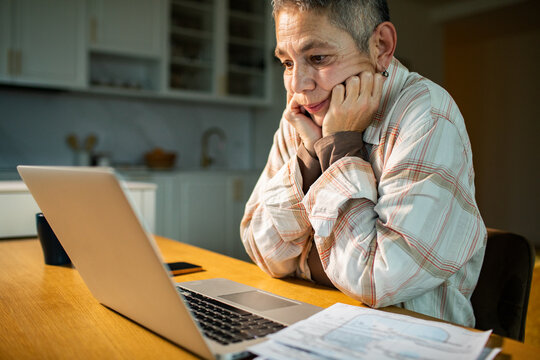 Older adult reviewing bills on laptop in home kitchen