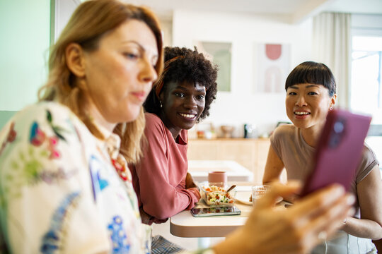 Three women looking at smartphone during lunch at home kitchen