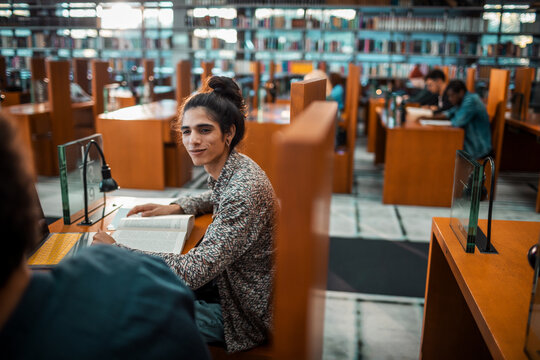 Smiling student studying with book in university library