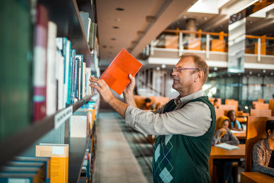 Middle aged man selecting book in library reading room