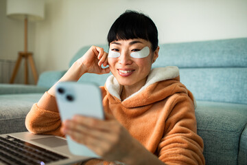 Smiling woman at home with under eye patches using smartphone © Geber86