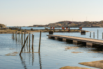 Fototapeta premium Wide coastal harbor scene with wooden piers calm water rocky islands and small structures in distance.