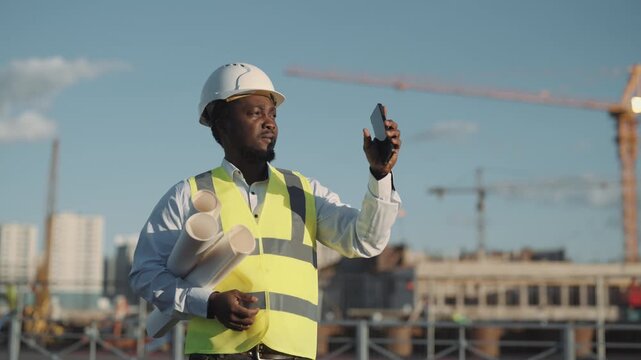 Portrait of successful architect or foreman in construction site, using phone. Online communication with departments in building site, african american man testing mobile application, medium shot
