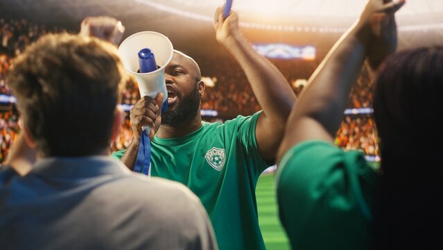 African american man chants through megaphone in football stadium stands during match, fan leader galvanizing soccer supporters to create loud atmosphere and strong team support and team spirit.
