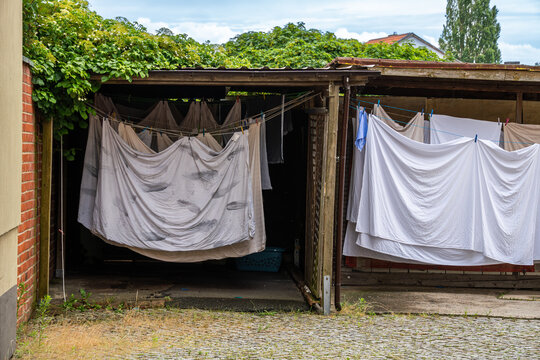 Freshly washed bed linen hangs on clotheslines under a carport, air-drying in a quiet courtyard