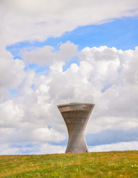 Modern wooden observation tower framed by clouds and grassy field.