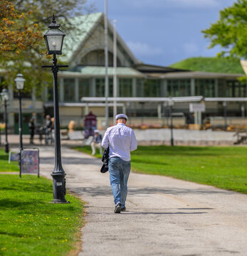Graduate in white cap walking through sunny park pathway.