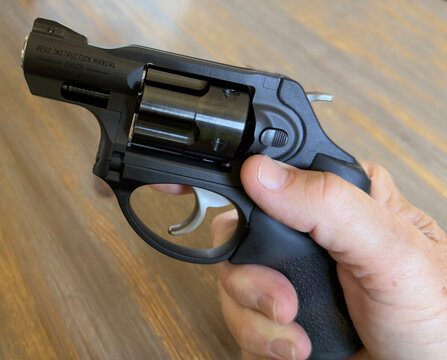 Close-up view of a male's hand holding a small revolver, finger placed along the frame to show safe trigger discipline and firearm handling