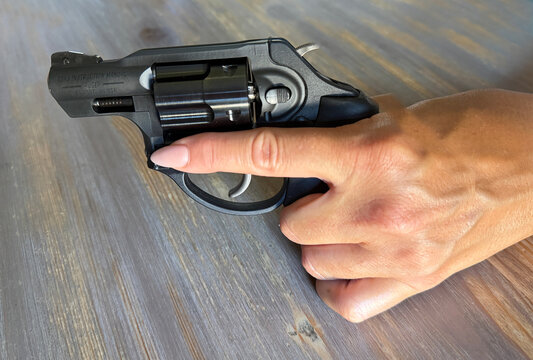 Close-up view of a female's hand holding a small revolver, finger placed along the frame to show safe trigger discipline and firearm handling