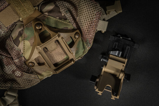 Detached tactical night vision mount lying next to multicam skull cap with integrated shroud on dark background close up