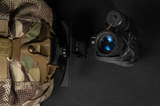 Top view of tactical night vision monocular with blue lens reflection attached to shroud on multicam skull cap on dark background