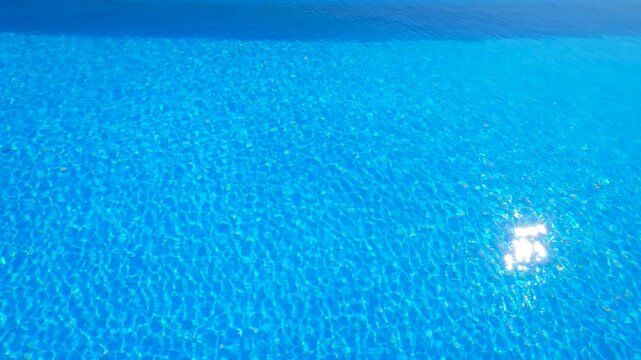Crystal clear swimming pool water rippling. Brilliant blue swimming pool water gently rippling and creating a caustic pattern on the bottom, with the sun's reflection sparkling on the serene