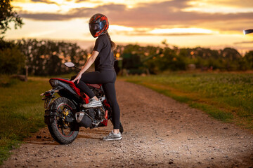 Obraz premium Girl biker resting on motorcycle at sunset on dirt road