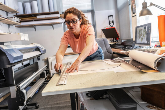 A print shop worker is preparing vinyl cutouts for application, carefully arranging them on transfer film. The process is clean and precise, focused on readying the design for final installation.