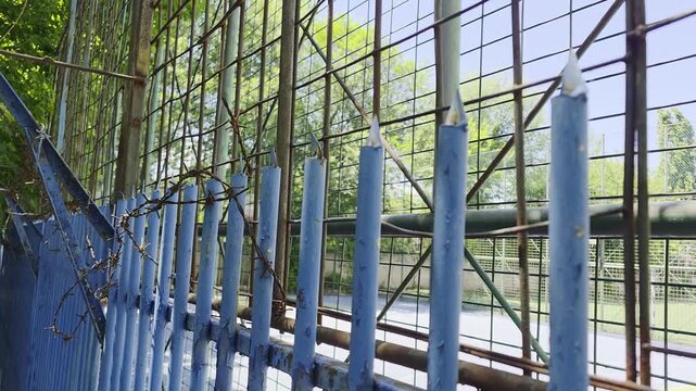 Old blue spiked metal fence with rusty barbed wire by a sports court