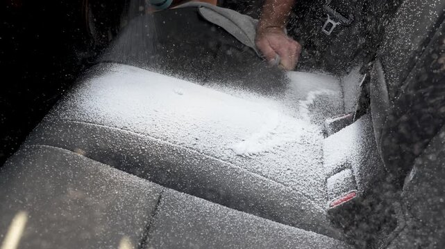Man spraying aerosol foam cleaner on fabric car seat close up. Car interior detailing, dry cleaning salon process, stain removal and vehicle maintenance concept.