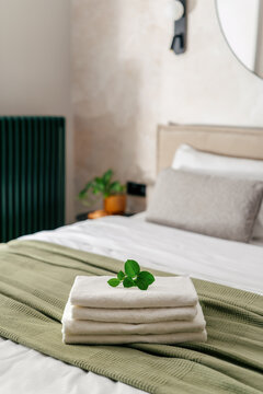 Hotel room features neatly folded white towels on the bed with a green textile accent