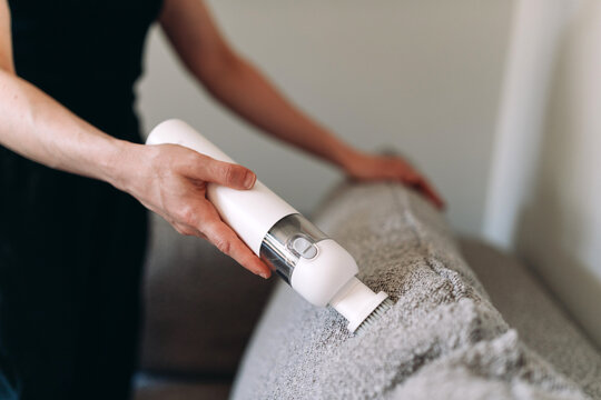 Woman uses cordless vacuum cleaner to clean couch in her home space
