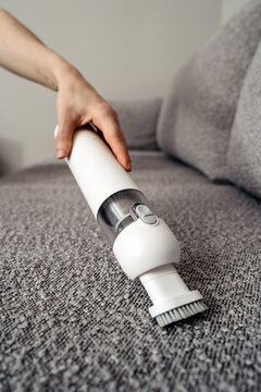 Woman uses cordless vacuum cleaner to clean couch in modern living room