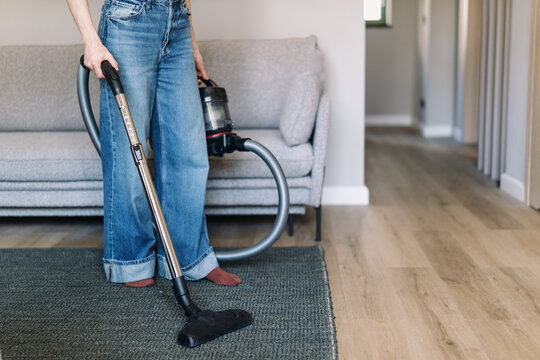 Woman cleans floor in living room with vacuum cleaner in modern apartment