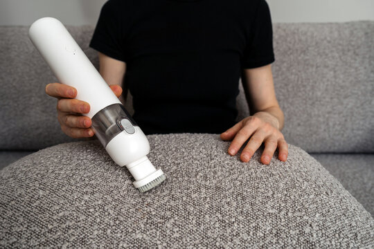 Woman cleans sofa with small cordless vacuum cleaner at home