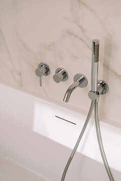 Freestanding bathtub with modern chrome faucet and marble walls
