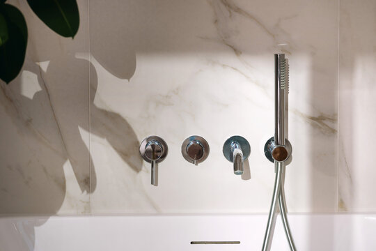 Sleek chrome shower head and faucet on white marble bathroom wall