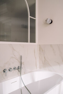 White freestanding bathtub in modern bathroom with marble tile walls
