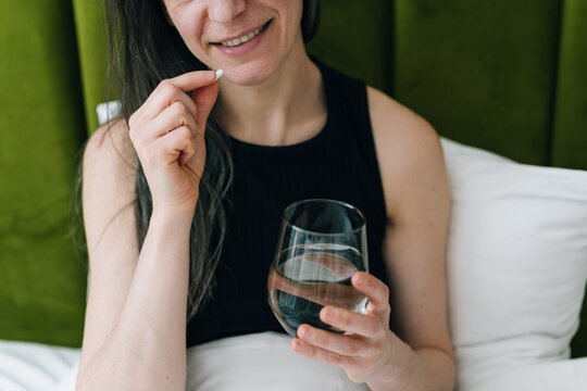 Woman takes a pill in the morning while sitting in bed with water