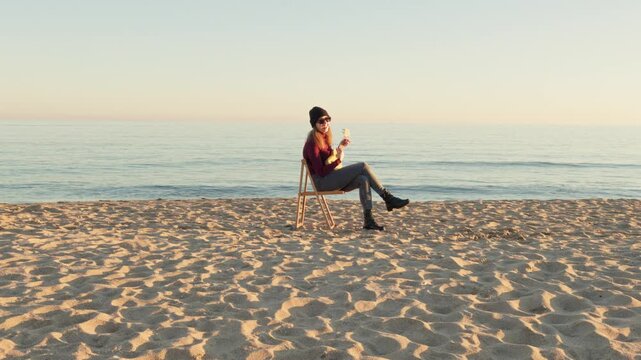 bohemian woman playing ukulele sitting alone on sandy beach
