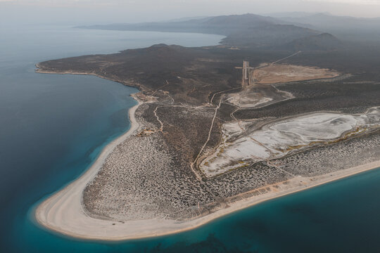 Aerial view of the sandy coastline and turquoise waters of the Sea of Cortez, featuring arid desert terrain and sparse vegetation in La Ventana, Baja California Sur, Mexico.