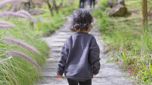 A young toddler confidently walks up a stone path in a lush park, embarking on a journey of independent discovery and childhood development through nature.
