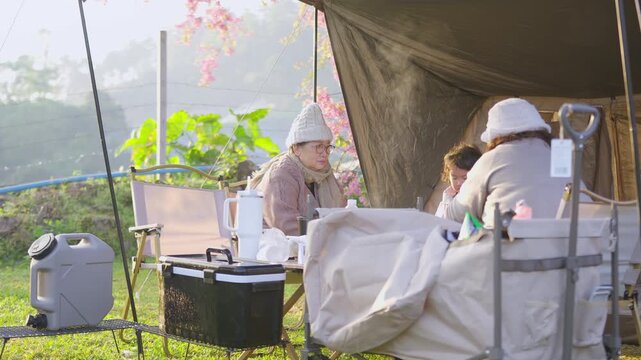 A multi-generation family unwinds with a warm drink at their campsite, enjoying quality time and the tranquility of an outdoor lifestyle during their vacation.
