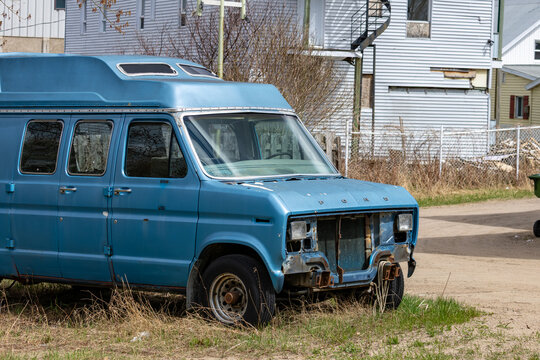 La Tuque, Quebec, 15 May 2026 : An old, light blue Ford van with a missing front grille and bumper sits in a grassy area.