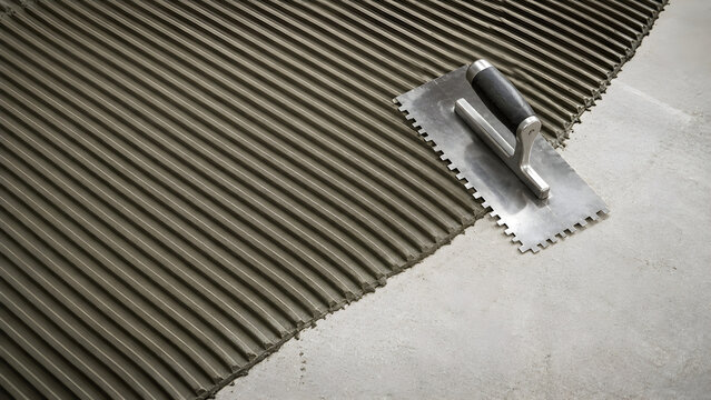 Notched Trowel Spreading Tile Adhesive on Floor Surface for Professional Tile Installation