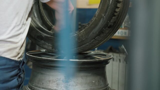 Professional car mechanic in a garage carefully fitting a new rubber tire onto an aluminum alloy wheel rim, preparing the wheel for balancing and seasonal vehicle maintenance