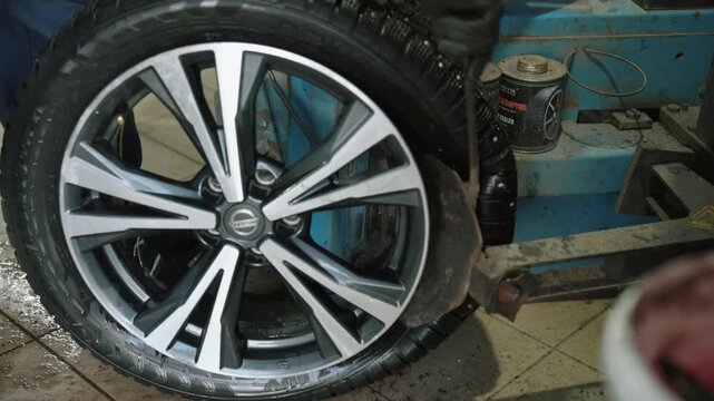 Professional mechanic performing tire mounting service in a workshop, replacing a winter studded tire with a summer one on a modern alloy wheel using specialized automated equipment