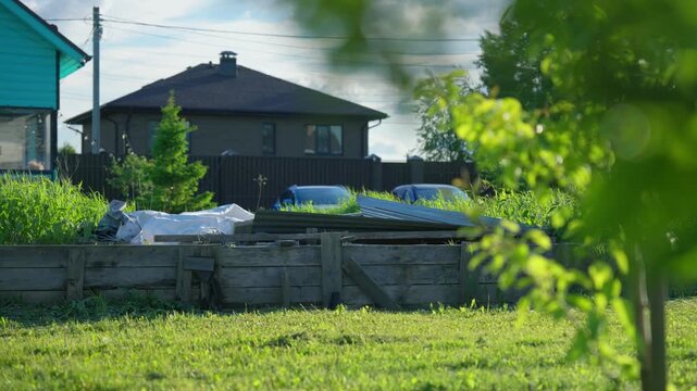 Sunlit green grass swaying in the gentle wind within a suburban backyard on a pleasant summer day, with a wooden fence and houses visible in the calm background under a cloudy sky