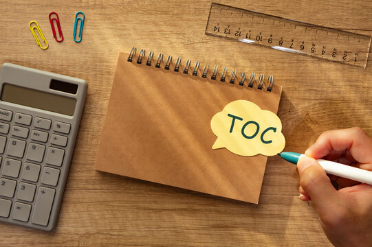 TOC theory of constraints &mdash; business process improvement concept with hand writing on sticky note, office desk with calculator