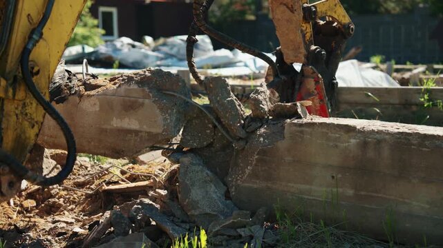 Heavy machinery with a jackhammer attachment breaking apart an old concrete block during demolition work on a construction site, crushing the material into rubble and creating dust