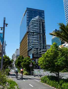 Cyclists pass modern glass towers in central Auckland as New Zealand's largest city invests in active transport infrastructure to reduce car dependency and meet climate emissions targets, Nov. 2025