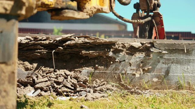 Close-up of concrete fragments falling from an old foundation during hydraulic demolition, showing rubble, structural removal and residential site preparation.