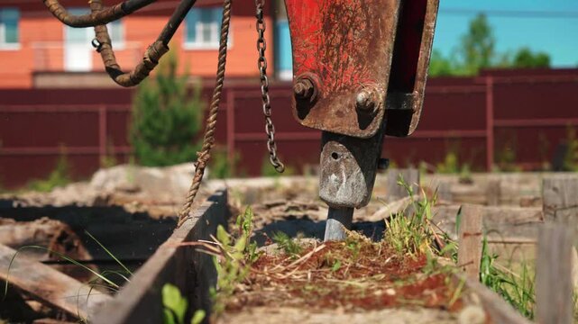 Close-up of hydraulic breaker working inside old wooden foundation formwork with grass and soil, showing demolition preparation, site cleanup and residential groundwork.