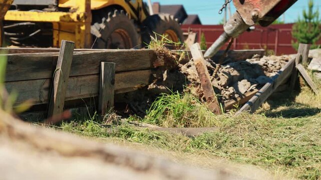 Heavy construction machinery with a powerful hydraulic hammer attachment breaking down an old wooden formwork structure and concrete foundation at a building site during demolition work