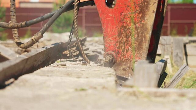 Heavy machinery with a hydraulic hammer breaking old concrete into pieces during demolition work on a construction site, with dust and rubble flying from the powerful impact on the foundation
