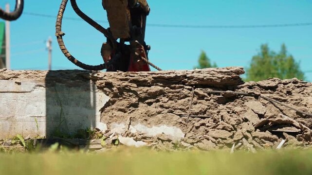 Professional demolition equipment with a hydraulic breaker attachment breaking down a reinforced concrete structure, creating rubble and dust against a clear blue sky on a sunny summer day